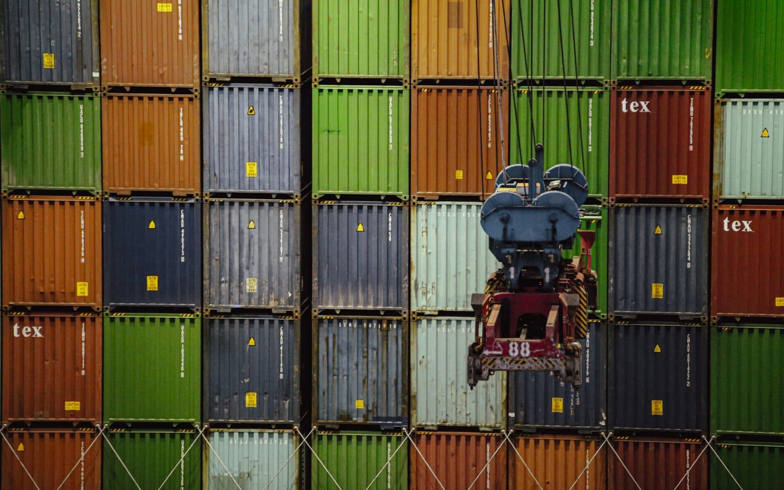 Palonnier de portique descendant devant un mur de portes de conteneurs empilés